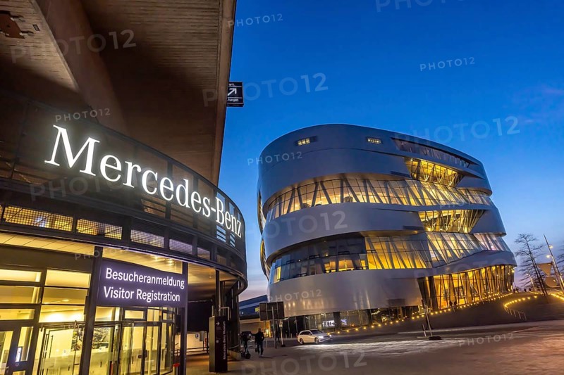 The Mercedes-Benz Museum in Stuttgart presents a journey through the automotive history of the global corporation. Spectacular architecture of the Automobile Museum in the evening. On the left, the entrance to the Mercedes-Benz Group AG factory premises. Stuttgart, Baden-Württemberg, Germany