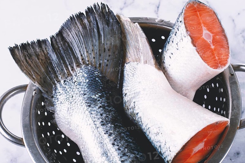 Fish tails are placed in a colander on a marble counter. The colander allows water to drain away from the fish. The fish looks fresh and clean, ready for cooking or preparation