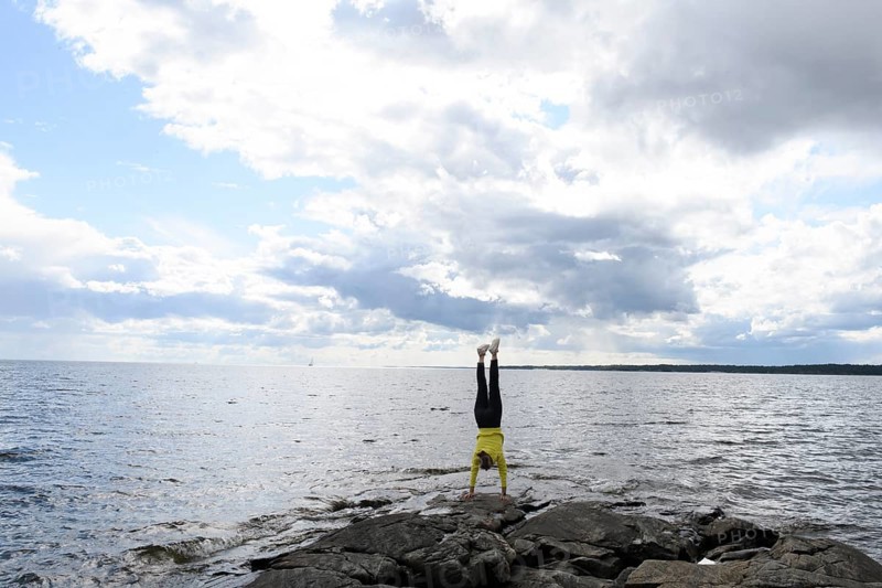 Young woman girl doing a handstand on rocks at Lake Vänern under cloudy sky, Värmlands län, Sweden