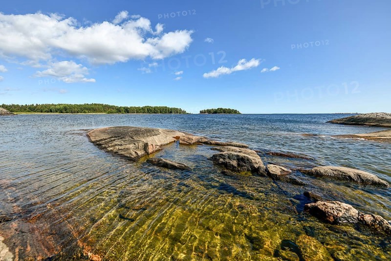 Clear sky over rocky archipelago coastline with granite archipelago with green forest and blue water at Lake Vänern, Värmlandsnäs peninsula, Värmlands län, Sweden