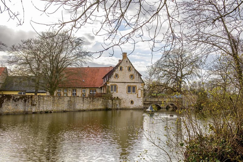 An old moated castle in Melle Haus Sondermühlen with bridge, surrounded by a large pond and trees Melle, Lower Saxony, Germany