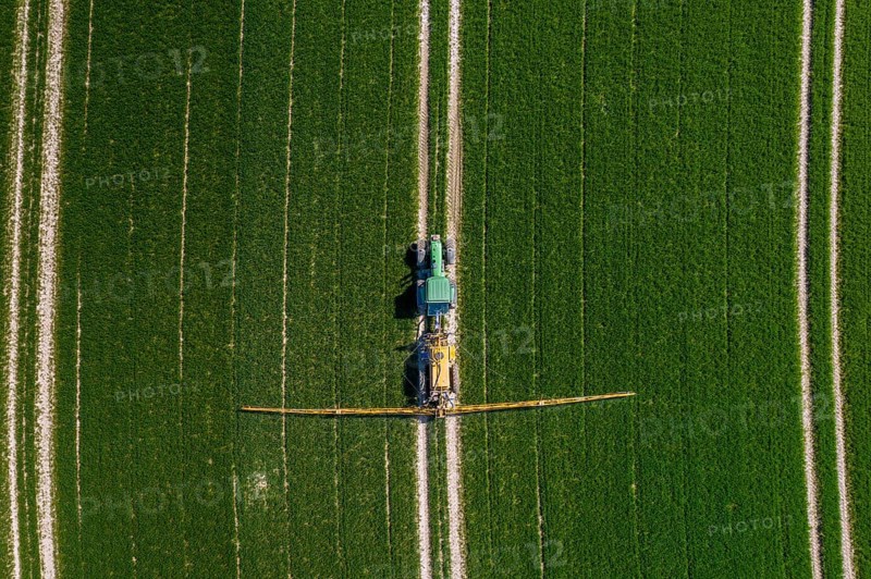Aerial view over agricultural trailed field sprayer pulled by tractor spraying crop on farmland, field with pesticides, insecticides in spring