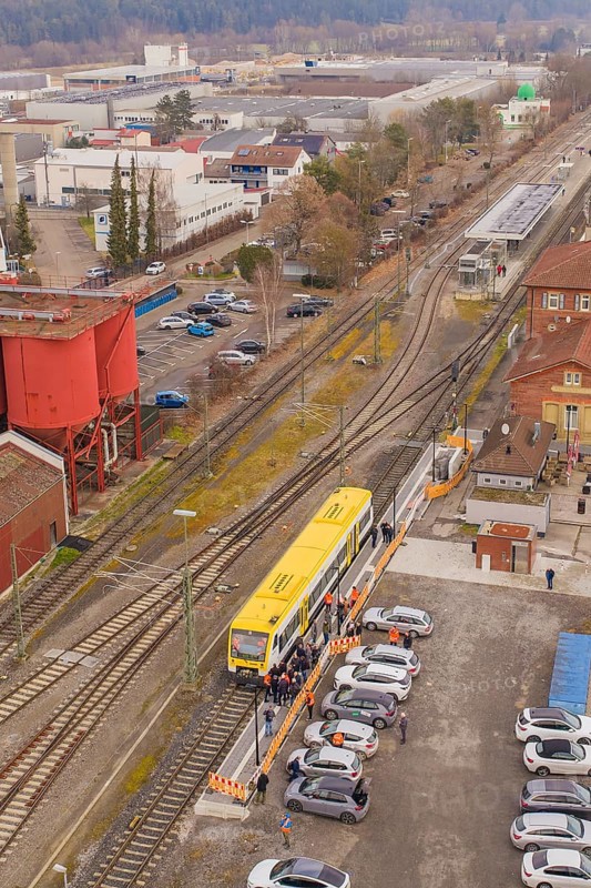 Yellow train at a train station surrounded by vehicles and buildings from a bird's eye view, taking the Hermann Hesse Railway, Calw, Black Forest, Germany