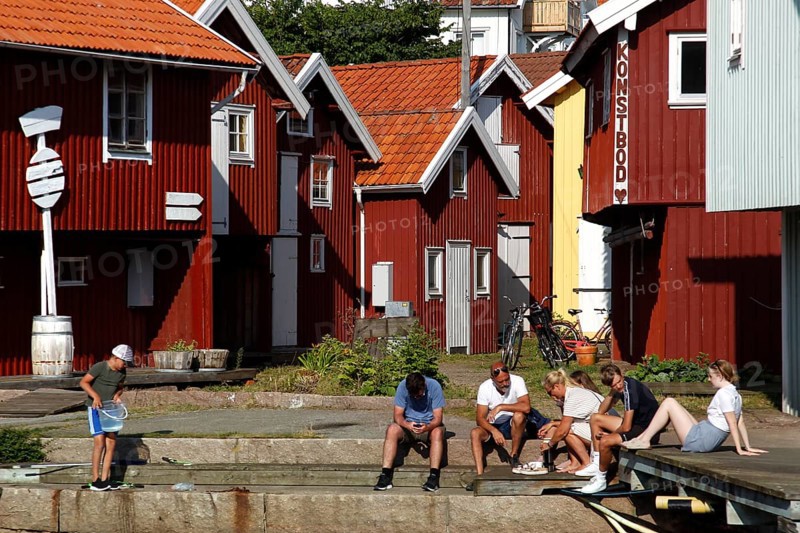 Group of people sitting in front of colorful wooden houses at the harbor, Smögen, Västra Götaland, Sweden