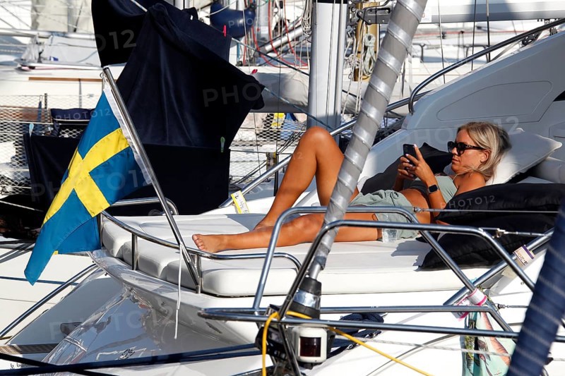 Woman relaxing on a sailboat with Swedish flag in harbor, Smögen, Västra Götaland, Sweden