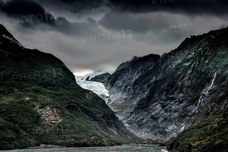 The Franz Josef Glacier with dramatic skies and steep, forested mountain slopes, Franz Josef, West Coast, New Zealand