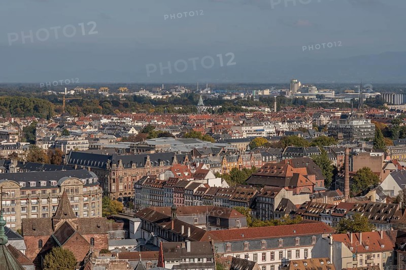 The stone balcony offers a view of the city of Strasbourg. Houses and buildings can be seen under a cloudy sky. Architectural details surround the balcony. Bas Rhin, Alsace, France