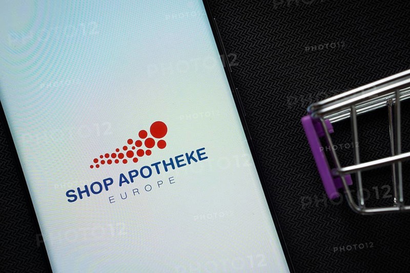 Dhaka, Bangladesh- 21 Nov 2025: A smartphone displaying the Shop Apotheke logo next to a miniature shopping cart on a background