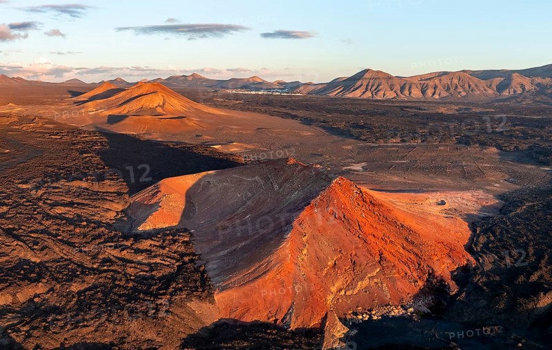Picturesque volcanic landscape in evening light, red volcano Montaña Bermeja between lava fields, aerial view, Lanzarote, Canary Islands, Spain