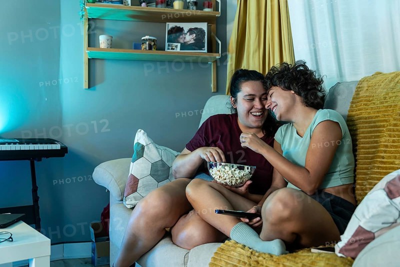 A joyful lesbian couple eating popcorn while watch tv, highlighting domestic harmony and love