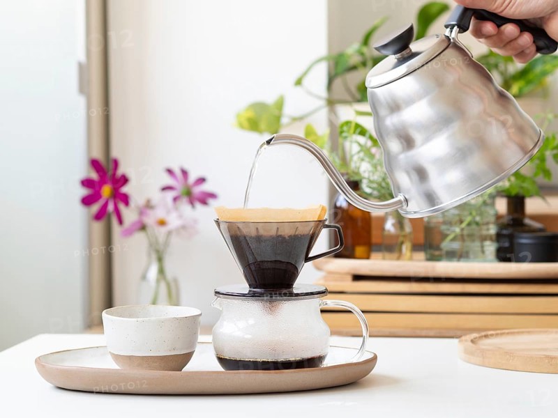 Barista preparing filter coffee using a modern kettle and a ceramic dripper