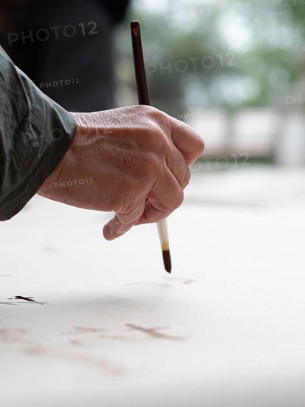 Hand holding a brush and painting on a white canvas during an ikebana workshop, creating floral arrangements