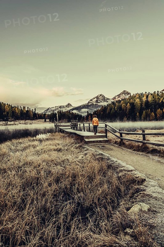 Young woman at Lake Staz near Sankt Moritz in the Engadine in Switzerland. Morning atmosphere with fog in autumn. Reflection of water