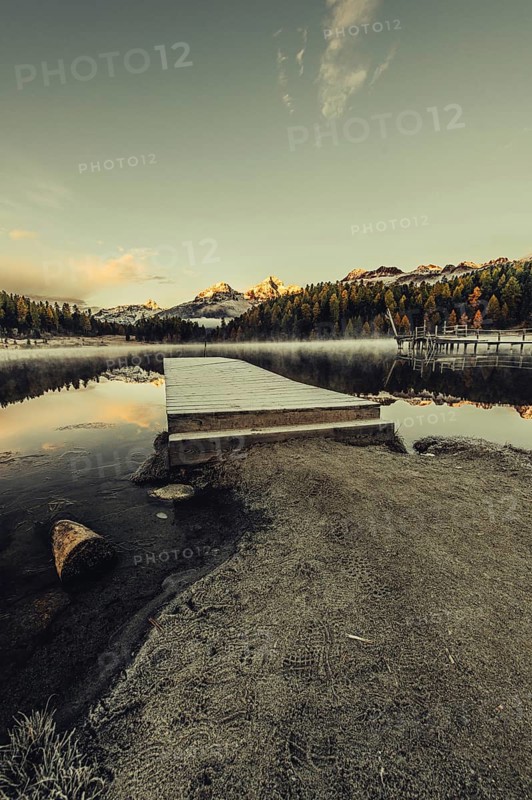 Lake Staz near Sankt Moritz in the Engadin in Switzerland. Morning atmosphere with fog in autumn. Water reflection and snow-covered mountains in the background