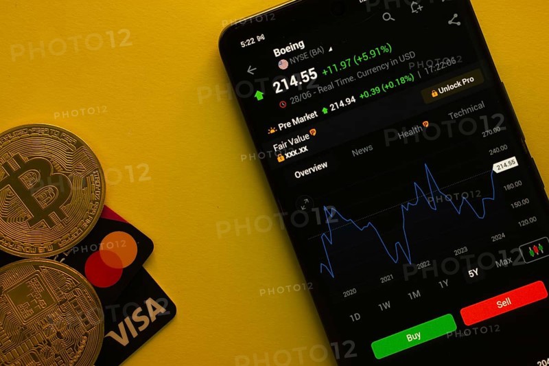 Dhaka, Bangladesh- 30 June 2025: Smartphone displaying Boeing stock data on a trading app with Bitcoin, Visa and Mastercard card on a vibrant yellow background