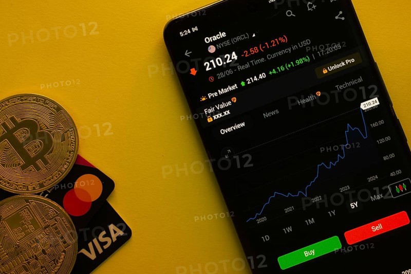 Dhaka, Bangladesh- 30 June 2025: Smartphone displaying Oracle stock data on a trading app with Bitcoin, Visa and Mastercard card on a vibrant yellow background
