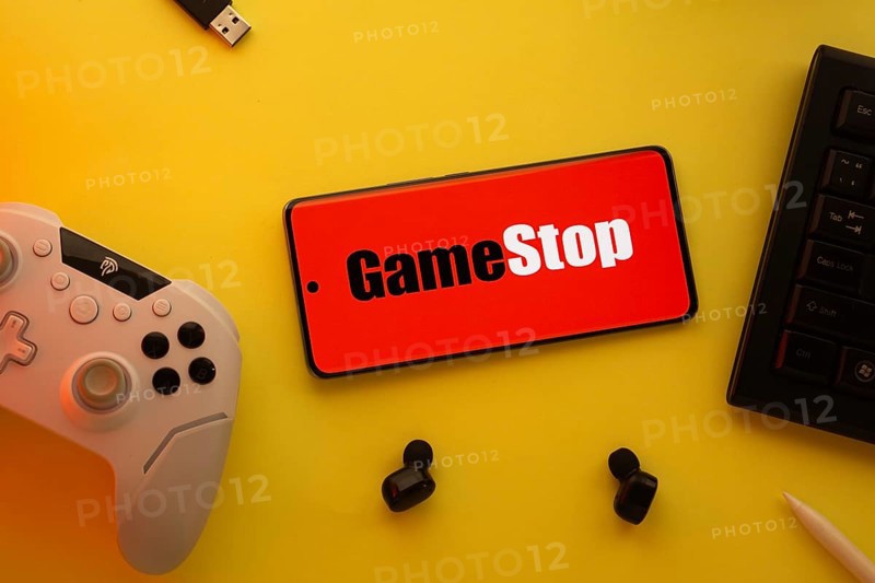 Dhaka, Bangladesh- 15 July 2025: Smartphone with GameStop logo, game controller, and earbuds on a yellow background