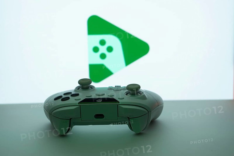 A close-up of a gamepad with the Google Play Games seen on screen in the background