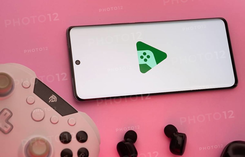 Smartphone with Google Play Games logo, game controller, and earbuds on a pink background