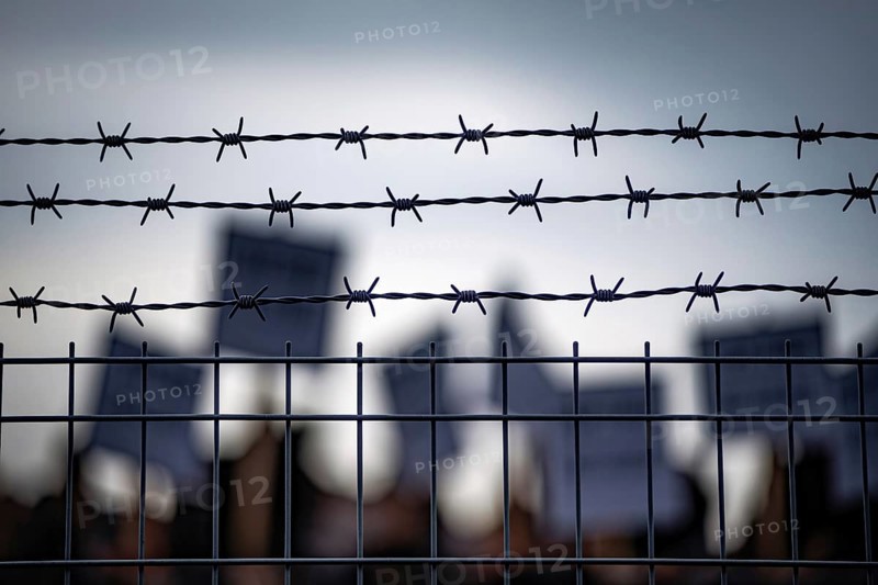 Barbed wire fence with blurred protesters and signs in background during border or prison demonstration Generative AI, AI generated
