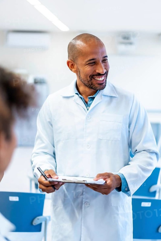 Friendly doctor holding a clipboard and smiling while talking with a patient in a hospital room