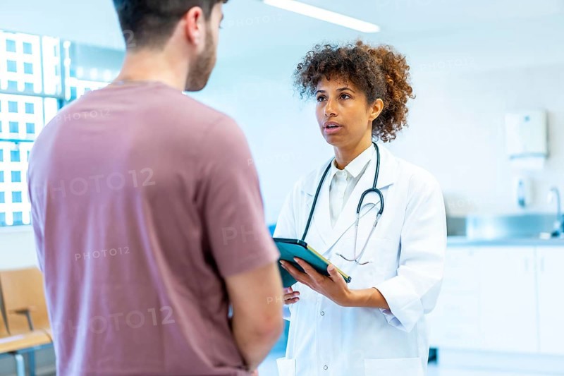 Doctor holding a tablet while explaining a diagnosis to a patient in a bright, modern hospital setting, fostering open communication and trust