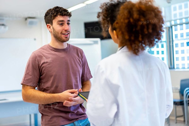 Young man holding a tablet, engaging in a conversation with a doctor inside a hospital room, discussing health and treatment options