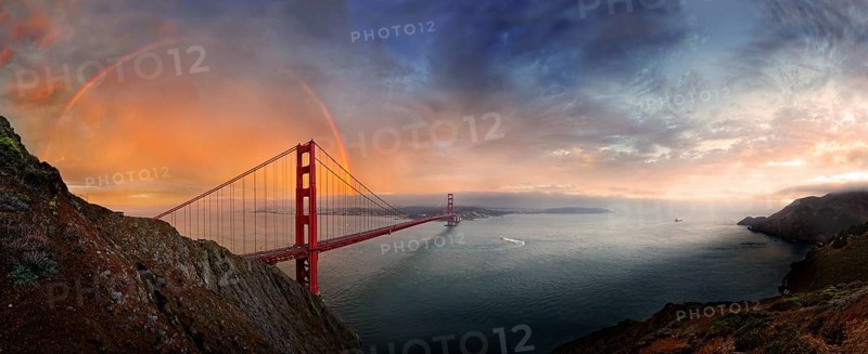 Panoramic view of the Golden Gate Bridge with a rainbow at sunset and orange-glowing storm clouds, San Francisco, California, United States