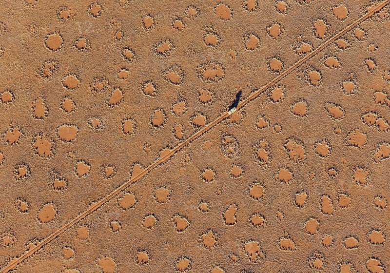 A vehicle of the balloon ground crew crosses a sandy plain with so-called Fairy Circles at the edge of the Namib Desert, photographed from a hot-air balloon, NamibRand Nature Reserve, Namibia