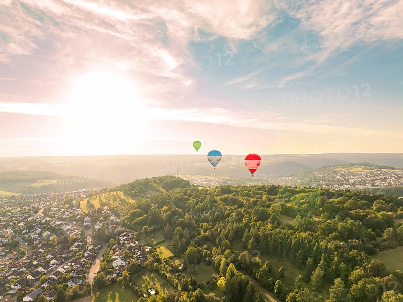 Hot air balloons float over a hilly and wooded landscape at sunset, Calw, Black Forest, Germany