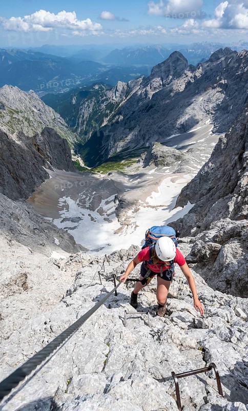 Mountaineer with helmet climbing in a secured via ferrata, Zugspitz via ferrata, ascent to the Zugspitze, view of mountain basin with snowfield of the Höllentalferner and Höllental, Wetterstein range, Wetterstein range, Bavaria, Germany