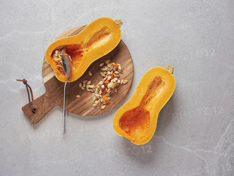 Remove the seeds from a raw butternut squash cut in half using a metal spoon. Cooking techniques and preparation of fresh vegetable ingredients