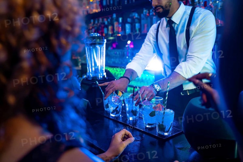 Professional bartender preparing cocktails at bar counter in nightclub, using fresh ingredients and garnishes