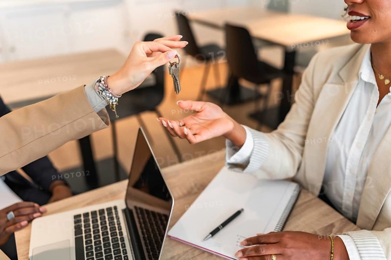 Businesswomen exchanging house keys after successful deal signing a contract in the office