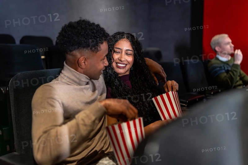 Happy couple enjoying a film in a cozy movie theater, sharing popcorn and laughing together, creating joyful memories on their night out