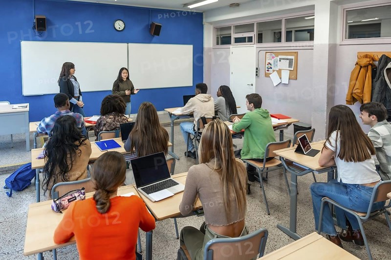 Multi ethnic group of high school students attending a lecture held by two teachers in a classroom at their university institute