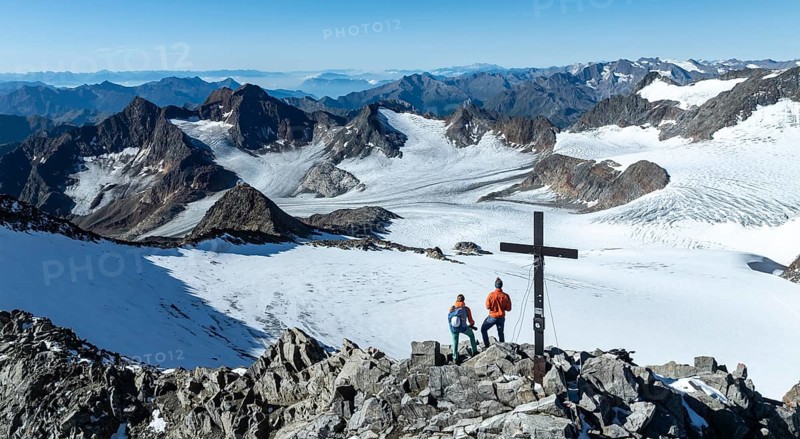 Panorama at the summit of the Wilder Freiger with summit cross and with glacier Übeltalferner and Wilder Freiger Ferner, two mountaineers at the summit in front of a spectacular mountain landscape, aerial view, Stubai Alps, South Tyrol, Italy