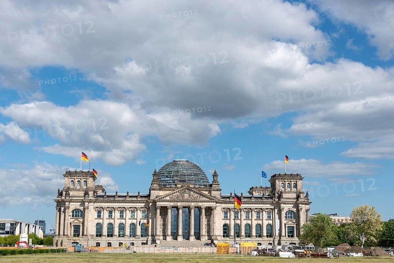 Front view of the Reichstag under a cloudy sky with waving flags, Berlin, Germany