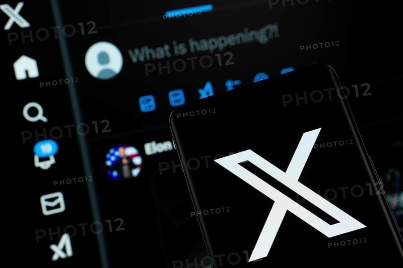 X (twitter) logo is seen on a smartphone, with the bluesky website visible on a computer screen in the background