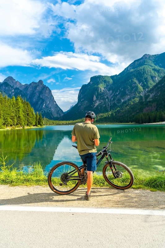 Mountain biker enjoying the breathtaking view of lake dobbiaco and the surrounding dolomites peaks on a sunny summer day