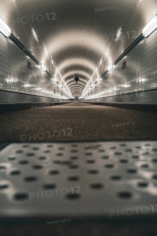 Long, illuminated tunnel with tiled walls from the ground perspective, old Elbe tunnel, Hamburg, Germany