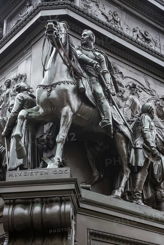 Historical equestrian statue of Frederick the Great at the Forum Fridericianum from 1839-1851, Hussar General Hans Joachim von Zieten in uniform with sword on a horse with eyes wide open and mouth agape from fear and pain, torture, cruelty to animals, artist: Christian Daniel Rauch, Berlin School of Sculpture, transition from Classicism to Realism, bronze, bronze sculpture, pedestal, portrait, imposing, equestrian monument, equestrian statue, sculpture, Berlin Mitte, City of Berlin, Germany