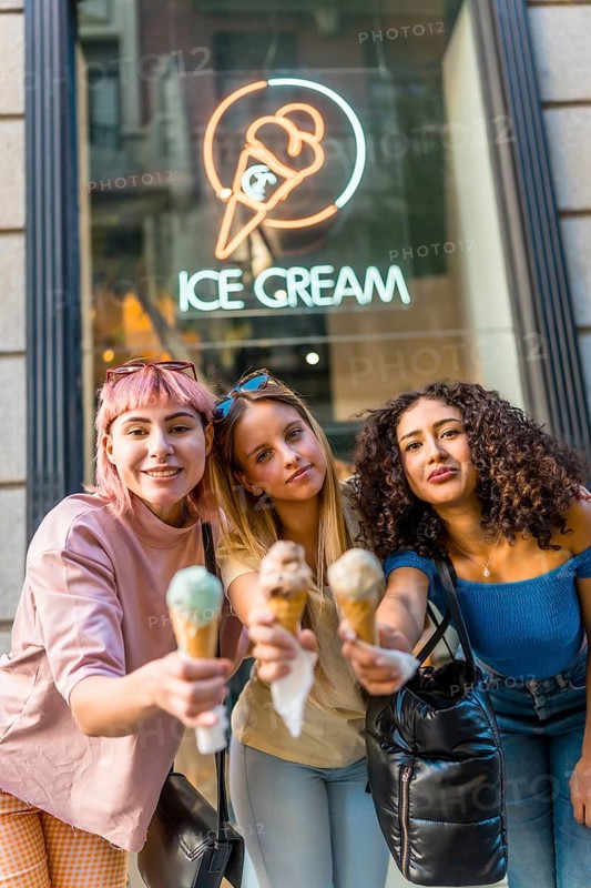 Vertical portrait of three diverse modern Women toasting with ice cream cones looking at camera in the street