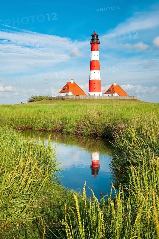 The Westerheversand lighthouse under a blue sky with white clouds reflected in a tideway, Westerhever, Eiderstedt peninsula, Schleswig-Holstein, Germany