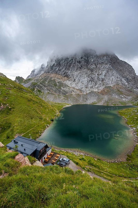 Alpenverinshütte Wolayerseehütte on Lake Wolayersee, cloudy mountain landscape with green meadows and mountain lake, Carnic Alps, Carnic High Trail, Carinthia, Austria