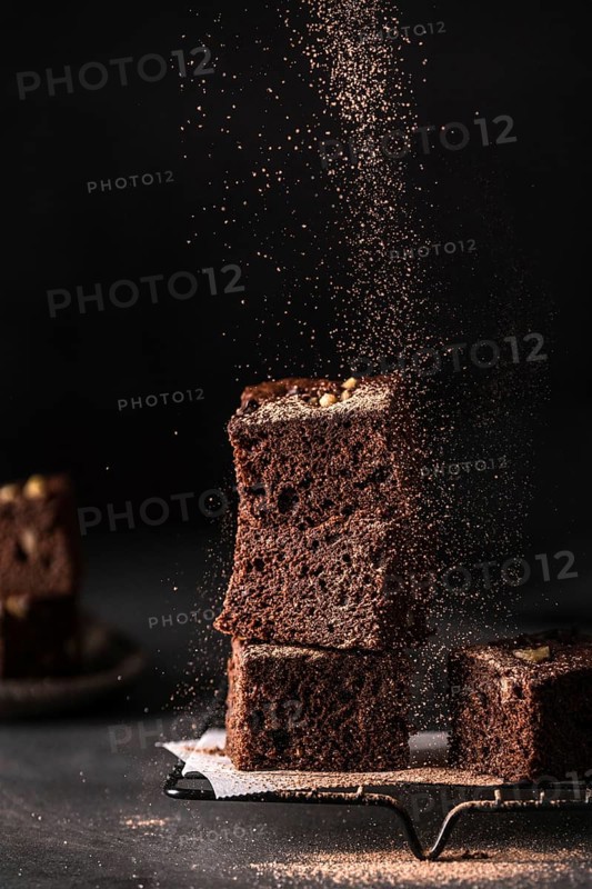 Composition of little stack of tasty sweet brownie cuts with powder on black background