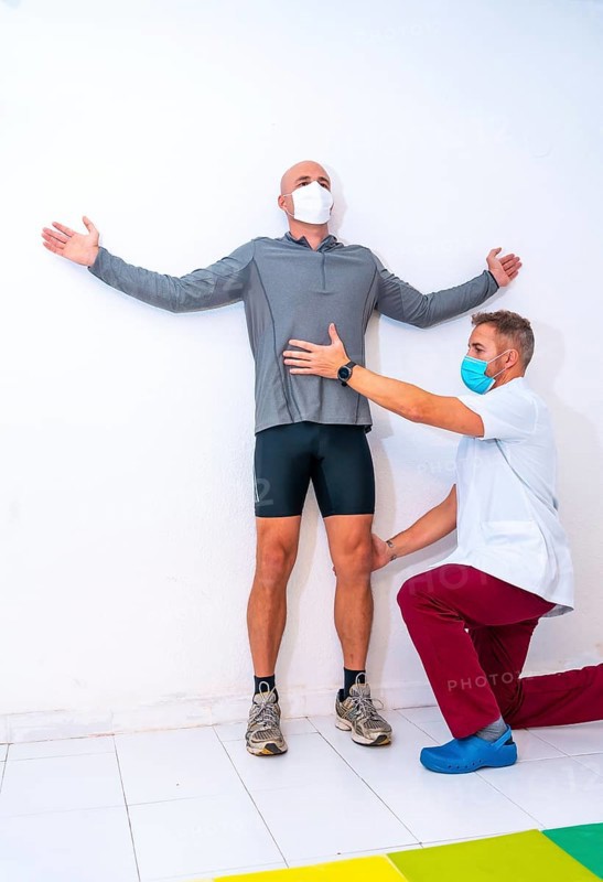 Physiotherapist with mask stretching client's neck with a hair on the wall. Physiotherapy with protective measures in the Coronavirus pandemic, COVID-19. Osteopathy, sports quiromassage