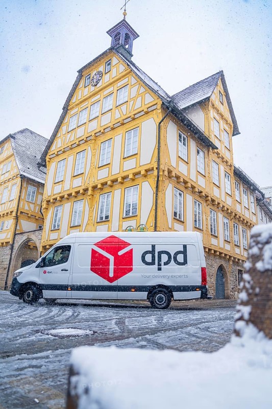 A DPD delivery van stands in front of a yellow-painted half-timbered building covered in snow, Sindelfingen, Germany