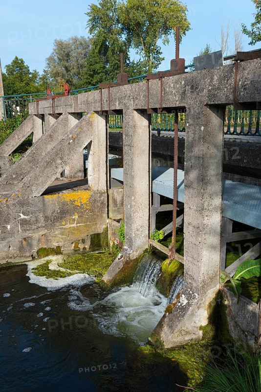 An old lock structure with concrete and masonry over which water flows, surrounded by trees, Cléry-sur-Somme, Cléry-su-Sonme, River Somme, Péronne, Hauts-de-France, France