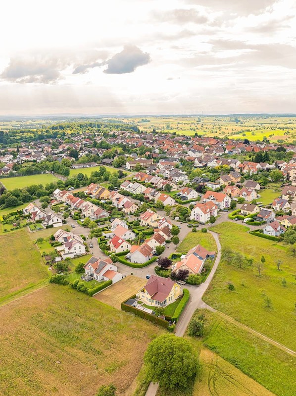 Residential area with densely built houses and streets, surrounded by fields under a slightly cloudy sky, Kieselbronn, Germany